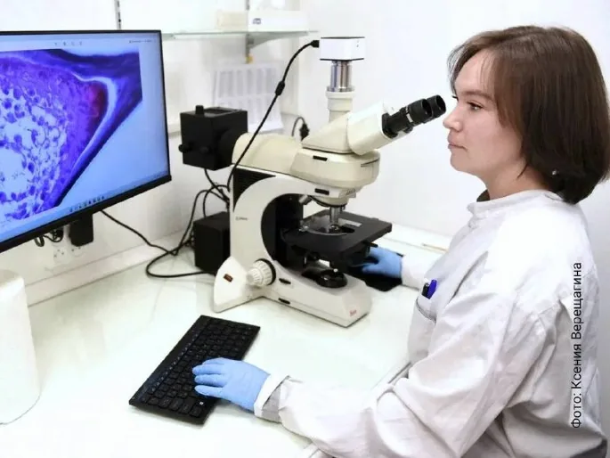 Исследовательница у микроскопа, на мониторе — изображение образца