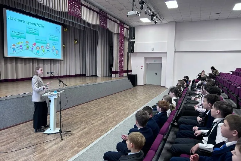 Лектор у трибуны в актовом зале школы, школьники слушают