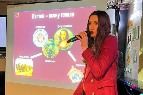 Исследовательница с микрофоном рассказывает о своей работе на фоне слайда